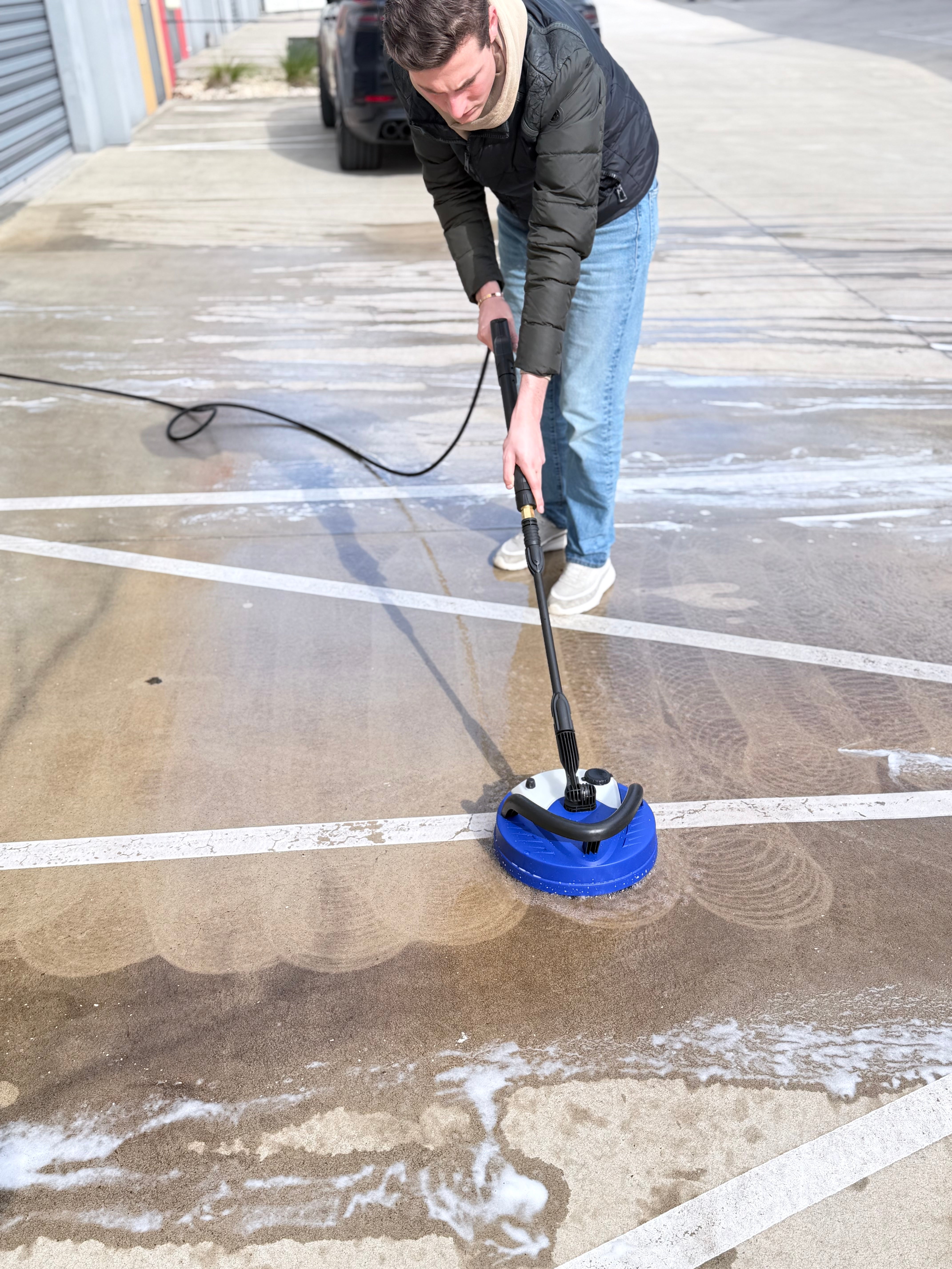 Close-up of the Annovi Reverberi patio cleaner in use — twin spinning pressure jets under the shroud lift dirt from concrete evenly with no overspray