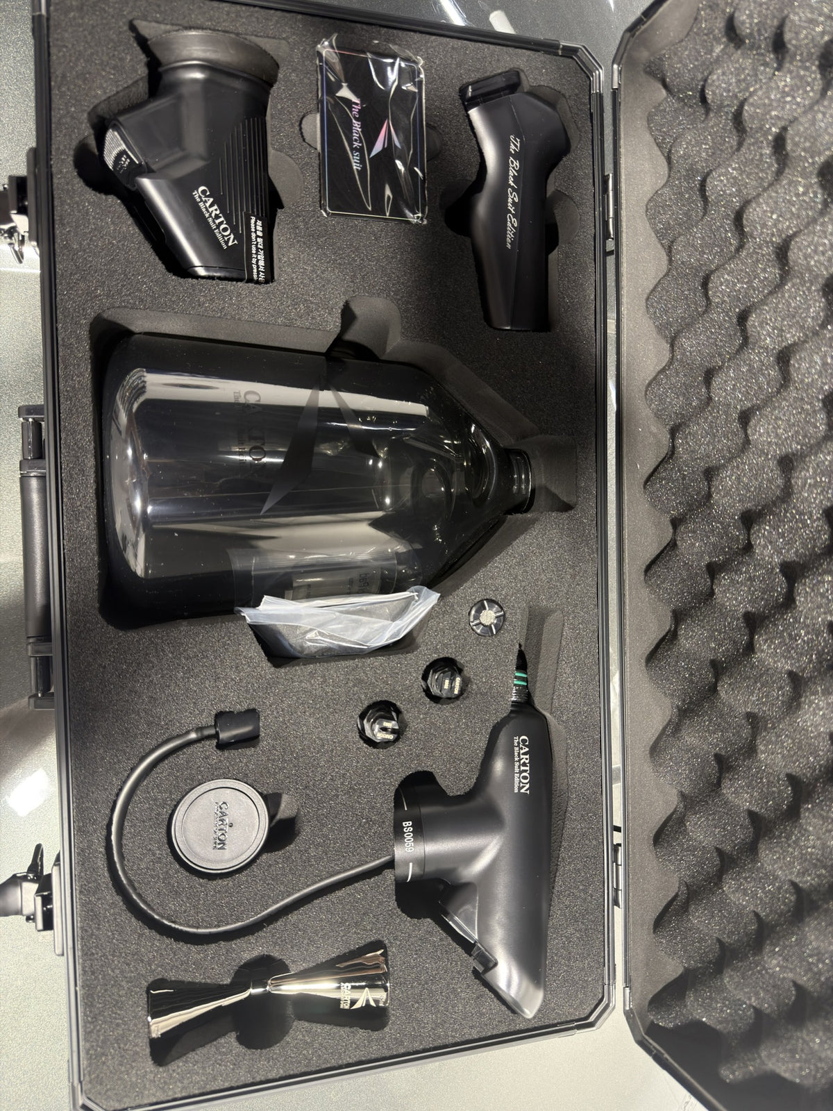 Carton Black Suit Edition kit contents - sprayer unit, battery handle, second head, 2.5L bottle, stainless jigger and fittings in foam cut-outs