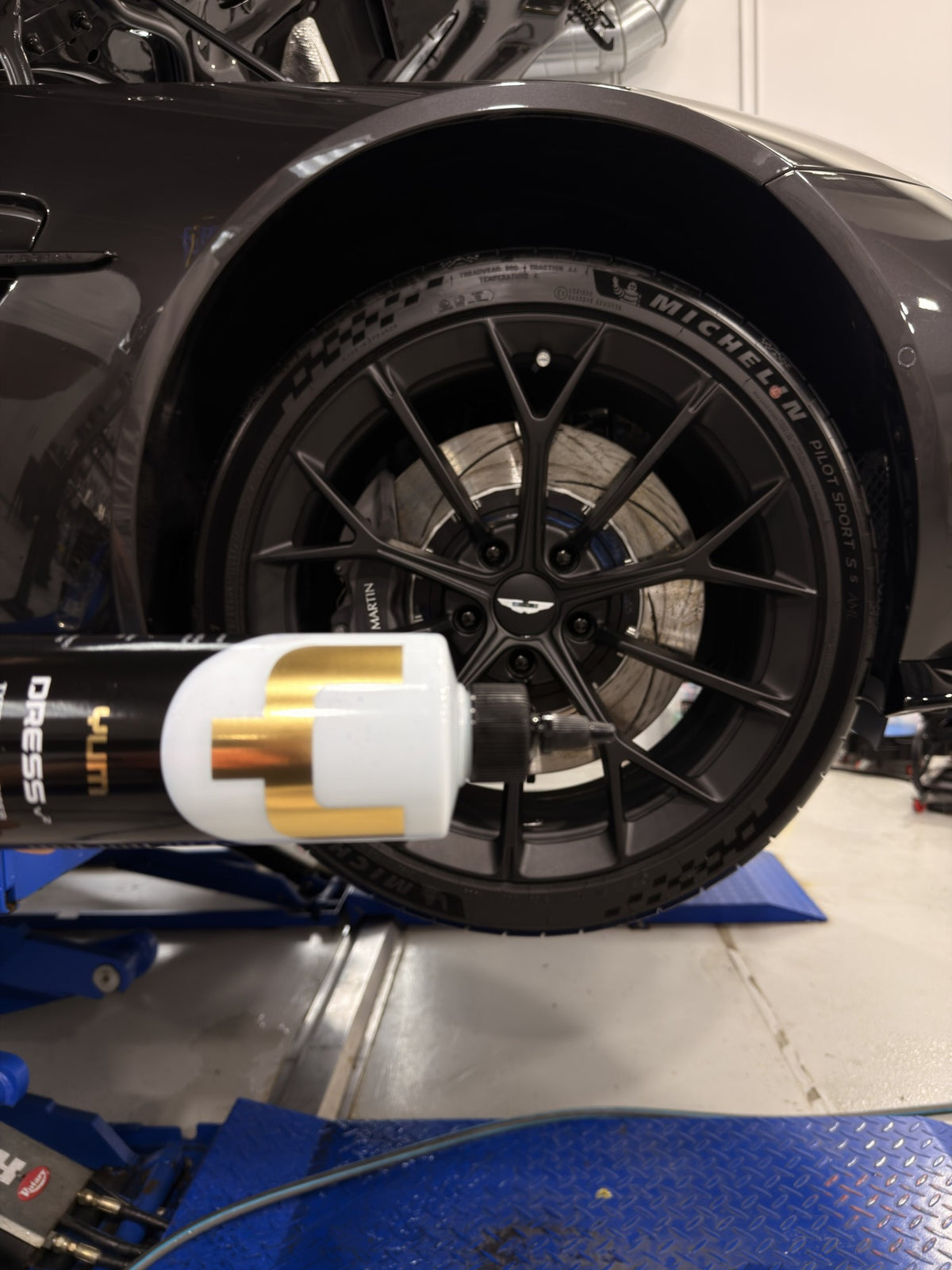 Yum Cars Dress V2 bottle held up to a satin black wheel and tyre at the Alpha Details studio